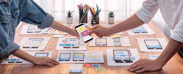 Panorama shot of frontend developer team brainstorming UI and UX designs for mobile app on paper wireframe interface User interface development team planning for userfriendly UI design Scrutinize