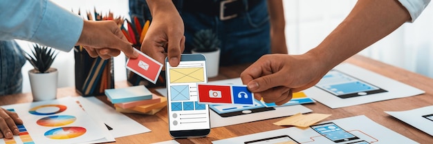紙のワイヤーフレーム インターフェイス上のモバイル アプリの UI および UX デザインをブレインストーミングしているフロントエンド開発者チームのパノラマ写真 ユーザー フレンドリーな UI デザインを計画しているユーザー インターフェイス開発チーム 精査