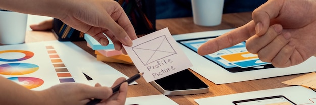 紙のワイヤーフレーム インターフェイス上のモバイル アプリの UI および UX デザインをブレインストーミングしているフロントエンド開発者チームのパノラマ写真 ユーザー フレンドリーな UI デザインを計画しているユーザー インターフェイス開発チーム 精査