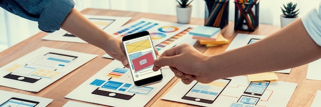 Panorama shot of frontend developer team brainstorming UI and UX designs for mobile app on paper wireframe interface User interface development team planning for userfriendly UI design Scrutinize