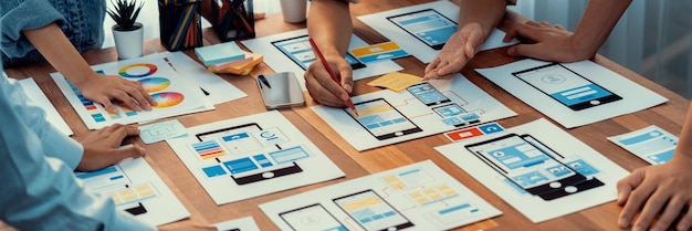 Panorama shot of frontend developer team brainstorming UI and UX designs for mobile app on paper wireframe interface User interface development team planning for userfriendly UI design Scrutinize