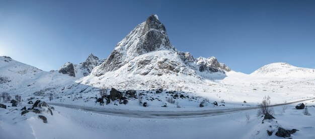 Panorama of snowy mountain range with blue sky and highway