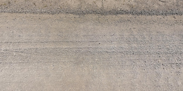 Panorama of surface from above curb of gravel road with car tire tracks