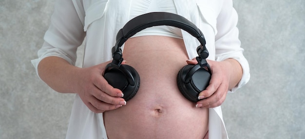 Panorama van een zwangere vrouw die muziek speelt voor haar baby via een koptelefoon die ze op haar buik legt