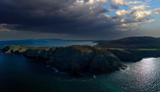 Панорамный вид сверху на скалистый выступ с камнями и растительностью, омываемый Черным морем в Болгарии под облачным небом