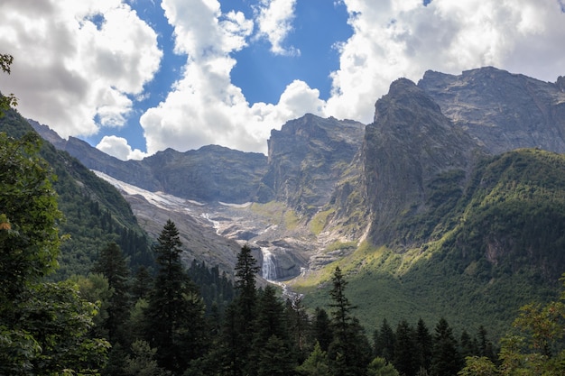 Panorama view on mountains scene and far away waterfall in national park of Dombay, Caucasus, Russia. Summer landscape, sunshine weather and sunny day