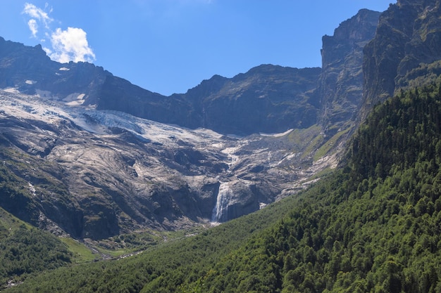 Panorama view on mountains scene and far away waterfall in national park of Dombay, Caucasus, Russia. Summer landscape, sunshine weather and sunny day