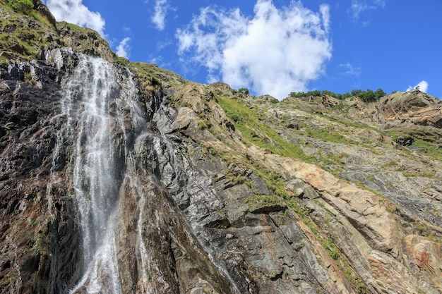 Panorama view of waterfall scene in mountains, national park of Dombay, Caucasus, Russia. Summer landscape, sunshine weather, dramatic blue sky and sunny day