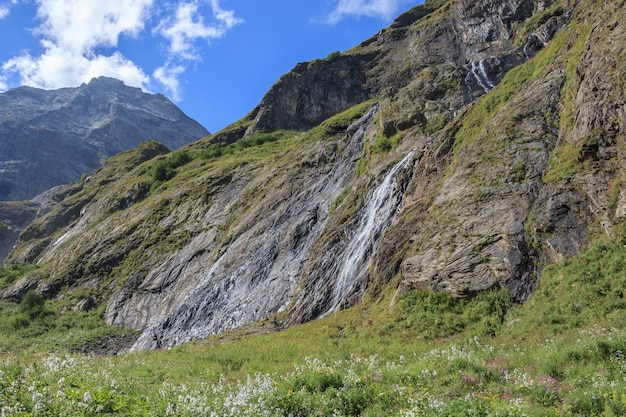 Panorama view of waterfall scene in mountains, national park of Dombay, Caucasus, Russia. Summer landscape, sunshine weather, dramatic blue sky and sunny day