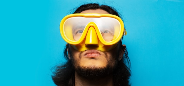 Panoramic banner view, close-up portrait of young man wearing yellow diving mask on blue background.