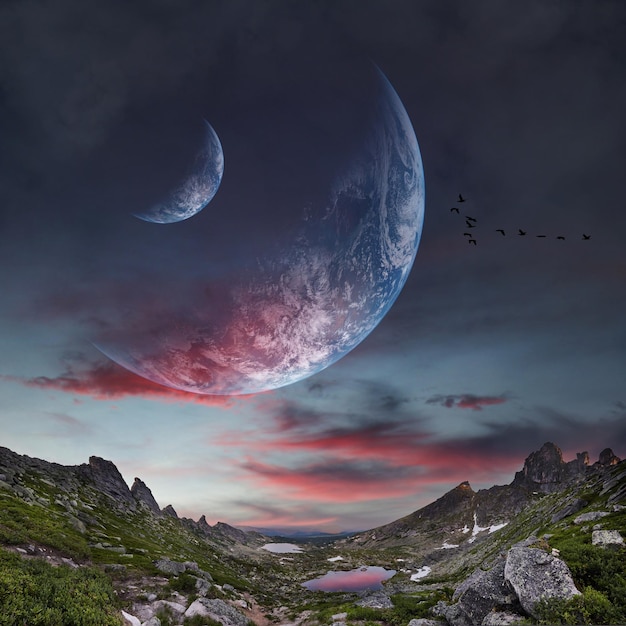 Panoramic mountains and two planets in sky. Fantastic world, birds flying against the background planets of moons. Sunset is reflected in clouds