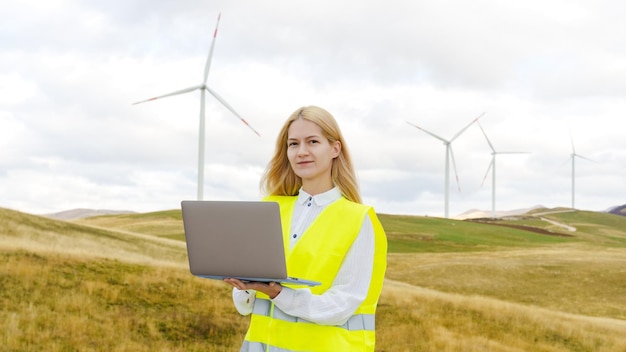 Photo panoramic photo of a female power grid engineer with a laptop against the background of wind turbines renewable energy