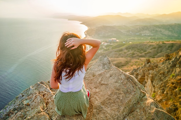 Panoramic photo of a happy woman who conquered the top of a cliff with a beautiful view of the sea