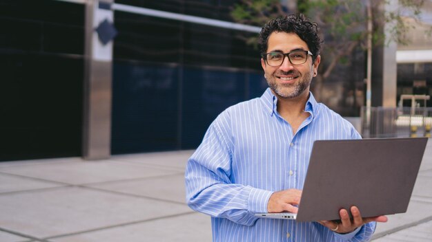 Panoramic photo of a middleaged latin man standing looking at camera with a laptop in his hands Copy space