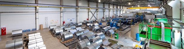 Panoramic photo shot of roll of painted galvanized steel sheet at cutting machine, ironworks and metalwork in factory. Industrial machine for metal sheet roof coils cut.