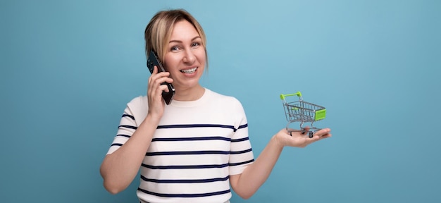 Panoramic photo of young cute casual woman shopaholic talking on phone holding empty shopping cart