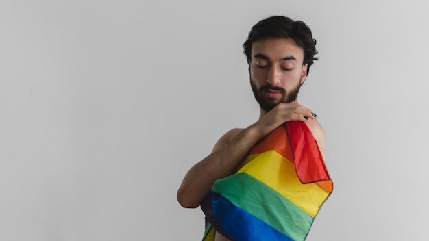 Panoramic photo of a young latin gay queer man embracing himself with the lgbt flag Copy space