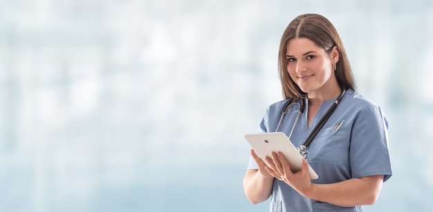 Panoramic photo of a young nurse in the hospital doing stuff on the tablet with stethoscope hanging on her neck.