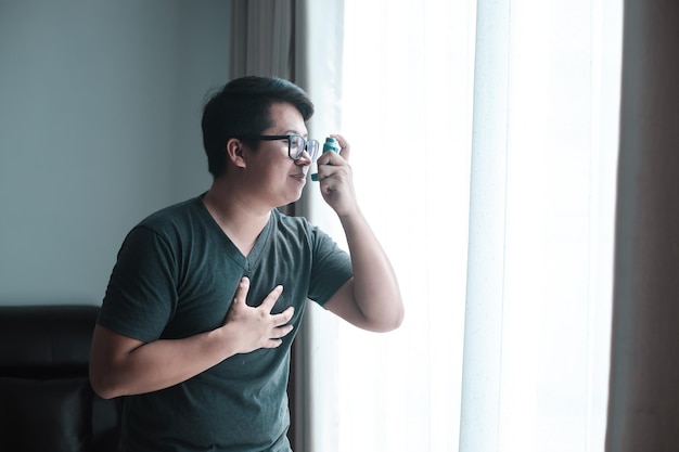 Panoramic shot of asthmatic man using inhaler with spacer Fat man using asthma inhaler while sitting at home due to allergy Asia man using spray asthma