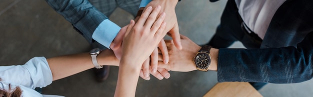 Panoramic shot of businesswoman and businessmen putting hands together