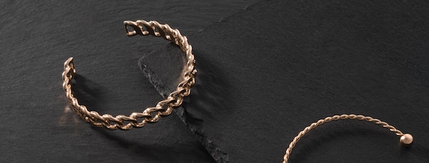 Panoramic shot of chain shape golden bracelet on black stone background with copy space