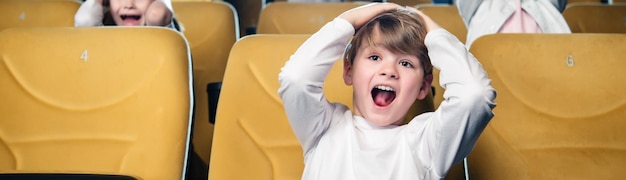 Panoramic shot of excited boy screaming while watching movie in cinema