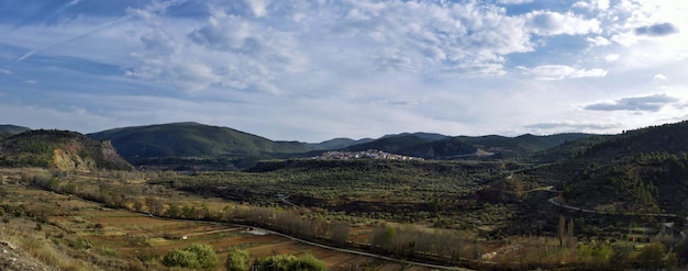 Panoramic shot of fields with trees and mountains under a cloudy sky