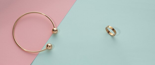 Panoramic shot of golden bracelet and ring on blue and pink paper with copy space