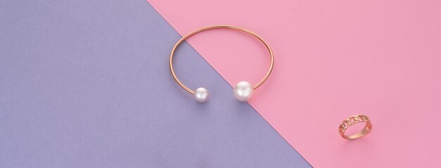 Panoramic shot of Modern gold bracelet and ring on pink and purple background with copy space