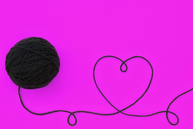 Panoramic top view of knitting black wool ball and thread in shape of heart on violet background. Wo