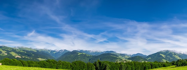 青い空の背景にある美しい緑の草原と山のパノラマ景色