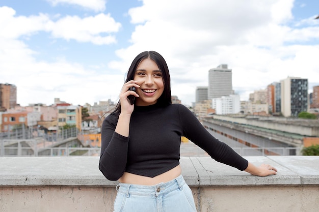 보고타(Bogota)의 한 테라스에서 전화로 통화하는 아름다운 여성의 탁 트인 전망과 콜롬비아(Columbia)의 도시 경관