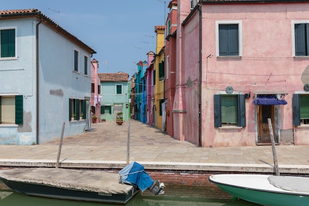 Panoramic view of brightly coloured homes and water canal with boats in Burano, it is an island in the Venetian Lagoon. Summer sunny day and blue sky