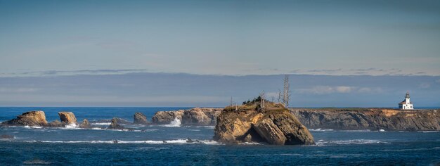 Panoramic view of the Cape Arango lighthouse in the distance and some rock formations in the foreground with a partly cloudy sky