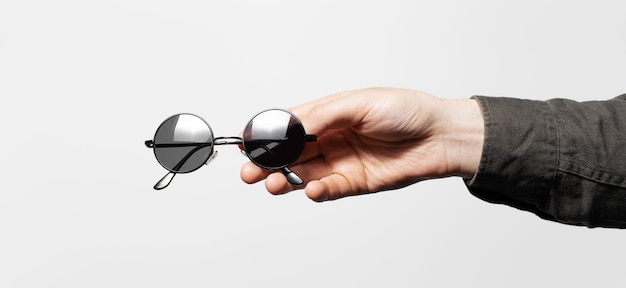 Panoramic view of male hand holding a round sunglasses on white background