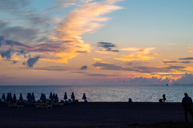 Photo panoramic view of mediterranean sea from beach with closed umbrellas and sunbeds against backdrop of colorful sunset of rhodes greece