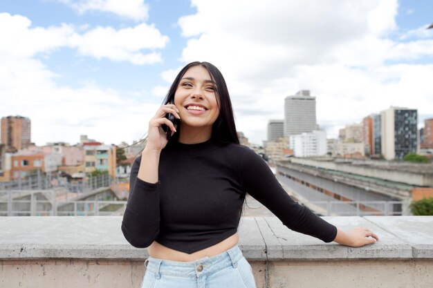 写真 コロンビアの街並みを背景に、ボゴタのテラスで電話で話している美しい笑顔の女性のパノラマビュー