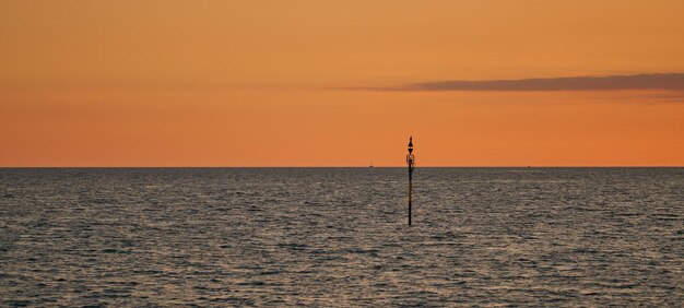 Панорамный вид на море с металлическим столбом и красивым закатом