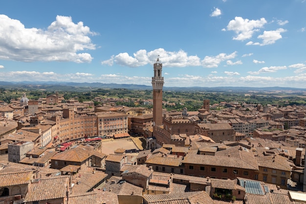 Panoramic view of Siena city with Piazza del Campo and the Torre del Mangia is a tower in city from Siena Cathedral (Duomo di Siena). Summer sunny day and dramatic blue sky