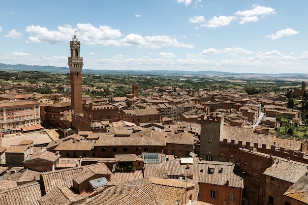 캄포 광장(Piazza del Campo)과 토레 델 망지아(Torre del Mangia)가 있는 시에나 시의 탁 트인 전망은 시에나 대성당(Duomo di Siena)에 있는 도시의 탑입니다. 여름 화창한 날과 극적인 푸른 하늘