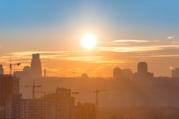 Vista panoramica del tramonto in città con silhouette di edifici e gru industriali