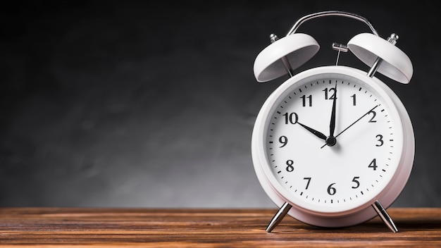 Photo panoramic view of white alarm clock on wooden desk against gray background