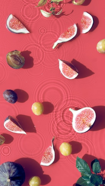 Panoramic water banner background Fresh ripe fig fruits and slices swimming in water Natural direct sunlight with shadows Ripples water rings on red background