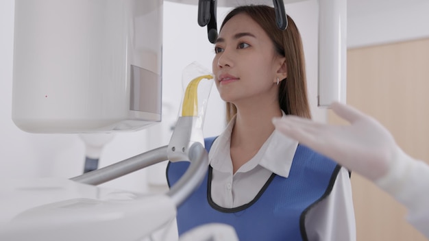 On a panoramic xray machine the dentist aligns the bite of a woman In a dental clinic a woman dressed in a lead apron stands still as a panoramic Xray machine circles her headxA