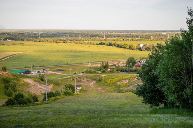 Panoramisch uitzicht vanaf de berg naar een kleine landelijke nederzetting tussen velden en bossen bij zonsondergang in de zomer.