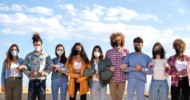 Panoramisch van multiraciale activisten die elkaars armen vasthouden en een barrière creëren met een beschermend gezichtsmasker dat protesteert op straat Demonstratieconcept