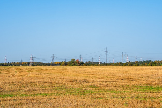 Panoramisch zicht op de hoogspanningslijn en de zendmasten die in een rij aan de horizon in het herfstveld staan