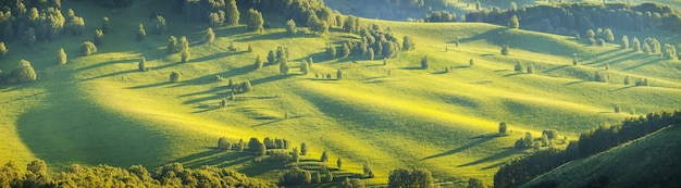 Panoramisch zicht op een schilderachtige vallei in het avondlicht, groene heuvels en weilanden