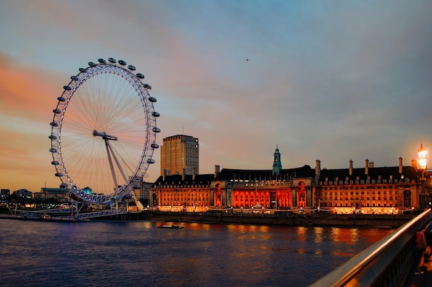 Panoramisch zicht op London Eye Ferris Wheel en County Hall aan de Thames River in de stad Londen in het VK in de avond. Skyline met beroemde icoon en plek voor reizen en cultuur. Bij zonsondergang. Vanaf de Westminsterbrug.