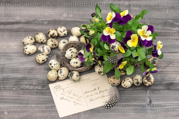 Цветы анютины глазки, перепелиные яйца и поздравительная открытка. пасхальное украшение